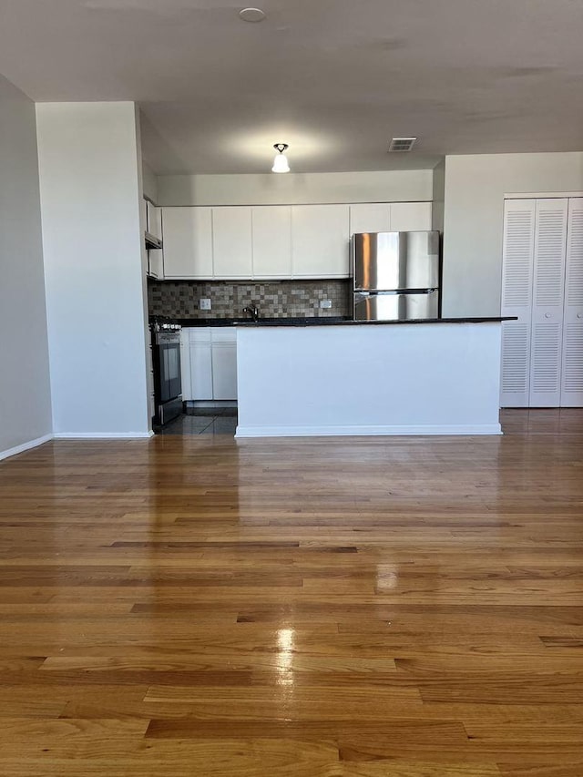 kitchen featuring gas stove, dark countertops, freestanding refrigerator, and white cabinets