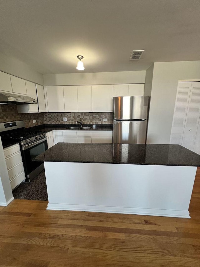 kitchen featuring appliances with stainless steel finishes, dark countertops, dark wood finished floors, and white cabinetry