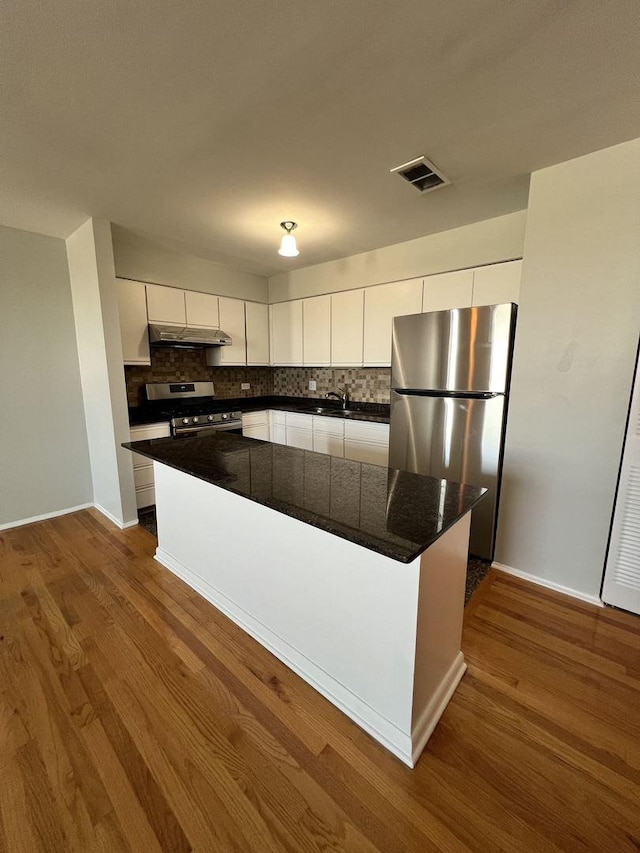 kitchen featuring dark wood finished floors, stainless steel appliances, dark countertops, white cabinets, and under cabinet range hood