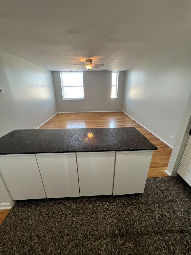 interior space with white cabinetry, baseboards, open floor plan, a ceiling fan, and light wood-type flooring