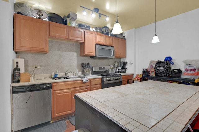 kitchen featuring tile countertops, appliances with stainless steel finishes, hanging light fixtures, sink, and decorative backsplash