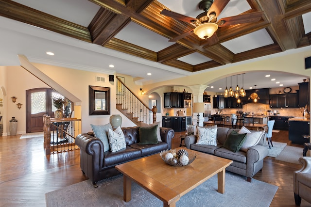 living room featuring ceiling fan, coffered ceiling, ornamental molding, and beam ceiling