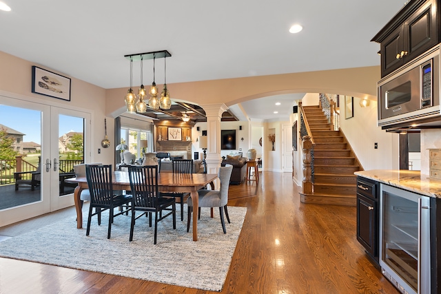 dining space featuring dark hardwood / wood-style floors, beverage cooler, french doors, decorative columns, and a notable chandelier