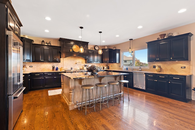 kitchen with appliances with stainless steel finishes, a center island, wood-type flooring, and pendant lighting