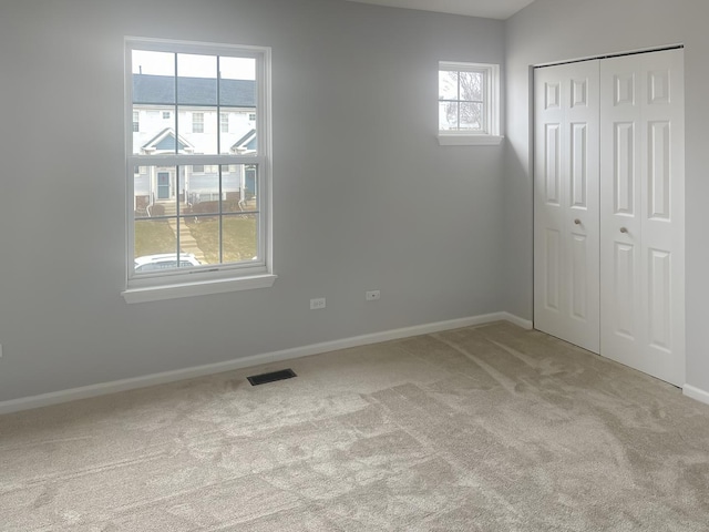 unfurnished bedroom featuring a closet, visible vents, light carpet, and baseboards