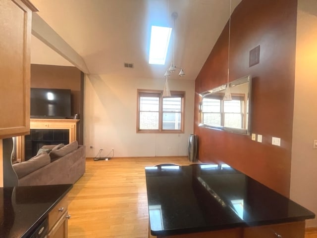 interior space featuring light hardwood / wood-style flooring, a tiled fireplace, high vaulted ceiling, and a skylight