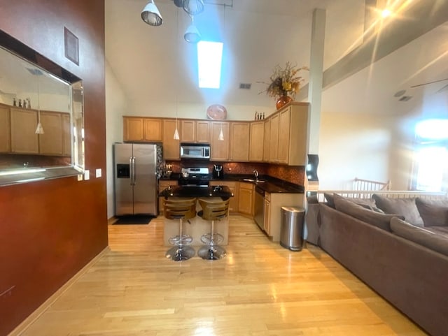 kitchen with a healthy amount of sunlight, appliances with stainless steel finishes, high vaulted ceiling, light wood-type flooring, and sink