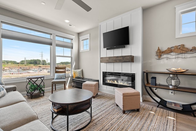 living room with light hardwood / wood-style floors, a fireplace, ceiling fan, and a healthy amount of sunlight