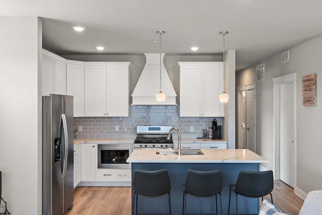 kitchen with appliances with stainless steel finishes, premium range hood, sink, light wood-type flooring, and light stone countertops