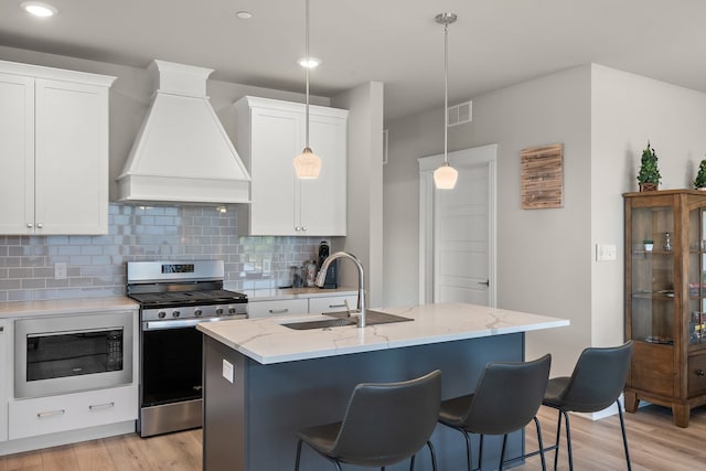 kitchen with black microwave, light stone counters, light hardwood / wood-style floors, stainless steel gas range, and premium range hood