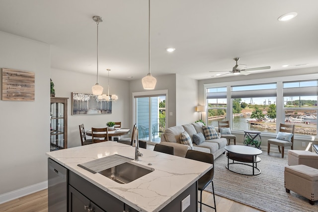 kitchen with dishwasher, light hardwood / wood-style floors, a kitchen bar, light stone countertops, and a kitchen island with sink