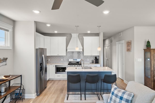 kitchen featuring light wood-type flooring, appliances with stainless steel finishes, custom exhaust hood, ceiling fan, and pendant lighting