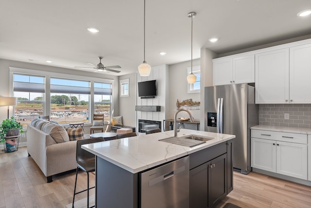 kitchen with appliances with stainless steel finishes, light hardwood / wood-style floors, sink, a center island with sink, and ceiling fan