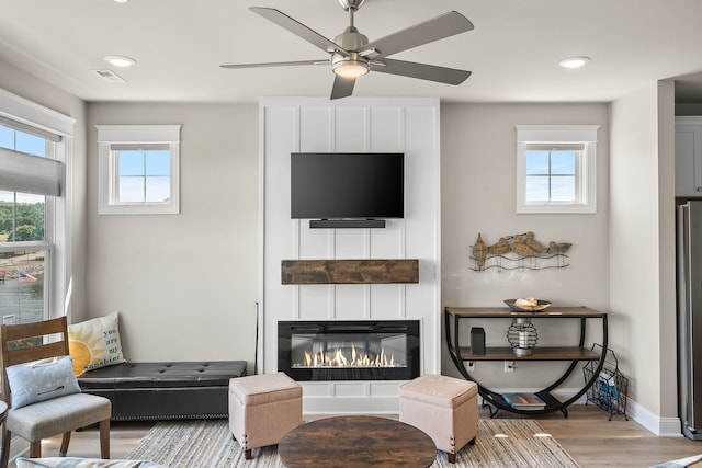 living room with ceiling fan, a large fireplace, and light wood-type flooring