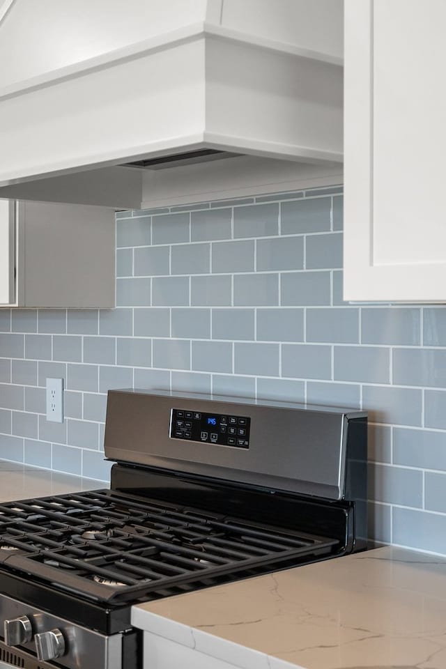 interior details featuring white cabinets, tasteful backsplash, light stone countertops, and stainless steel range with gas cooktop