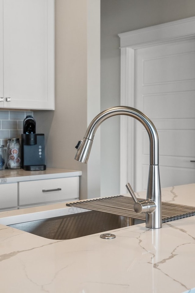 room details with sink, decorative backsplash, white cabinetry, and light stone countertops