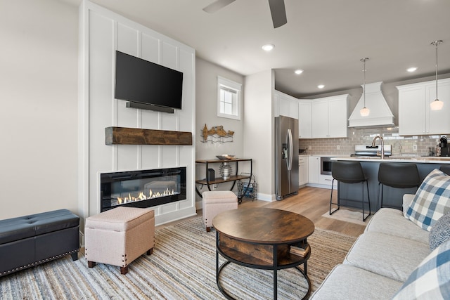 living room featuring light hardwood / wood-style flooring, ceiling fan, and a large fireplace