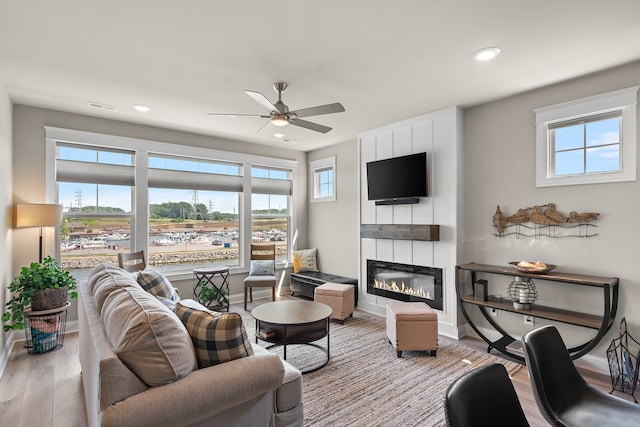 living room with ceiling fan, a large fireplace, plenty of natural light, and light hardwood / wood-style flooring