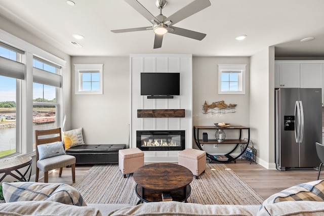 living room with light hardwood / wood-style flooring, ceiling fan, and a large fireplace