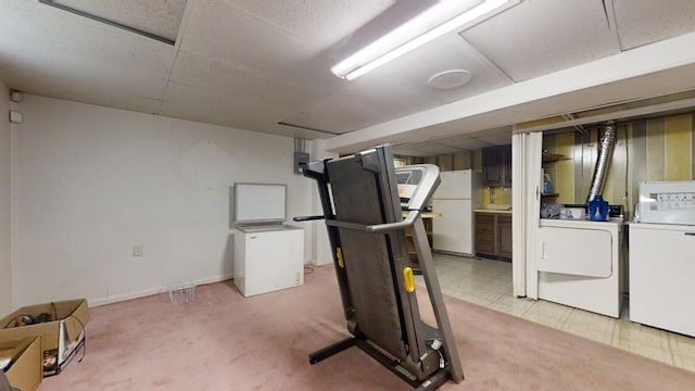 exercise room with light carpet, a paneled ceiling, and independent washer and dryer