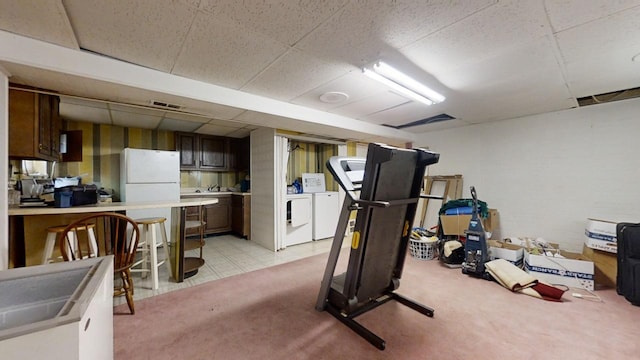 exercise room with light tile patterned floors, a drop ceiling, and washer and clothes dryer