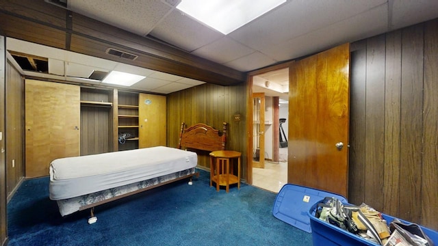 carpeted bedroom featuring a paneled ceiling, a closet, and wood walls