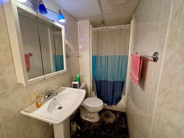 bathroom featuring tile patterned flooring, shower / bathtub combination with curtain, toilet, tile walls, and a drop ceiling