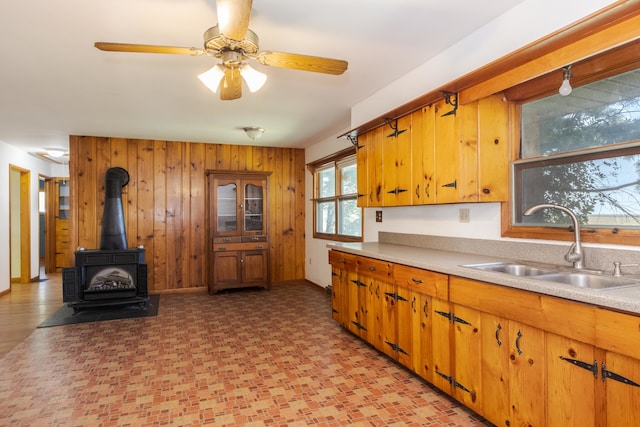 kitchen featuring a wood stove, ceiling fan, sink, and wooden walls