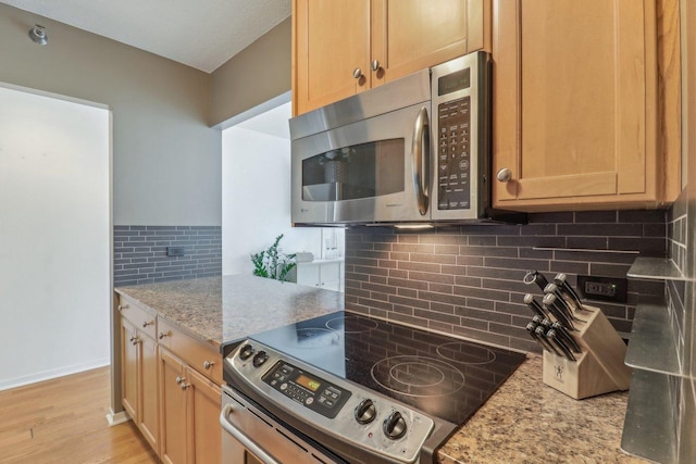 kitchen with light stone countertops, baseboards, stainless steel appliances, decorative backsplash, and light wood-type flooring