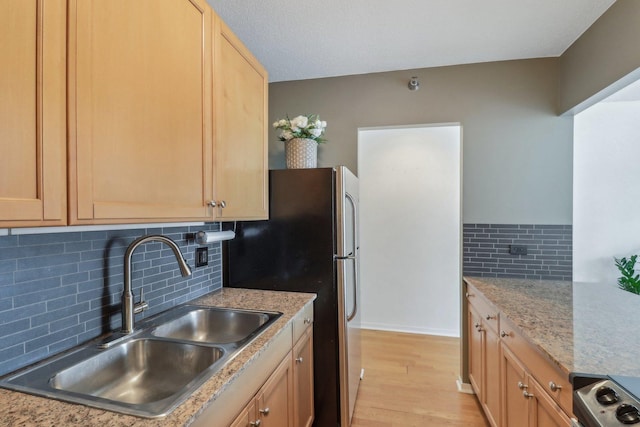 kitchen with light stone countertops, light wood-type flooring, backsplash, and a sink