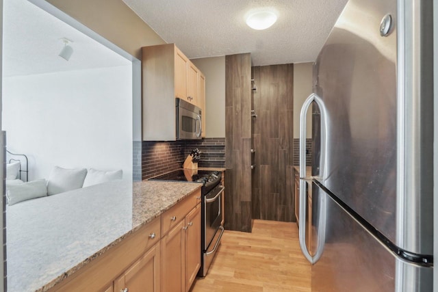 kitchen featuring light stone counters, light wood finished floors, stainless steel appliances, decorative backsplash, and a textured ceiling