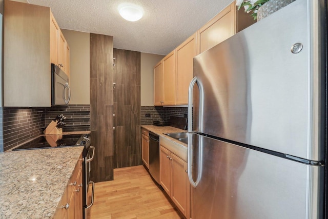 kitchen featuring light brown cabinets, light wood finished floors, stainless steel appliances, a textured ceiling, and backsplash