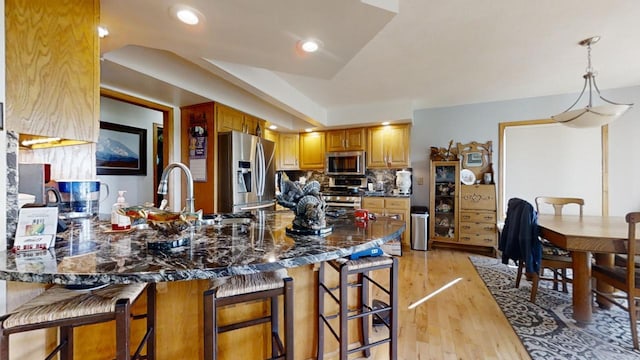 kitchen featuring tasteful backsplash, appliances with stainless steel finishes, a kitchen breakfast bar, dark stone counters, and light hardwood / wood-style flooring