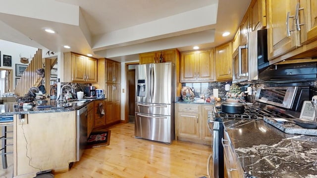 kitchen featuring light hardwood / wood-style flooring, dark stone countertops, stainless steel appliances, and backsplash