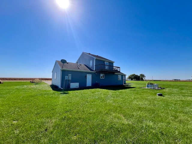 rear view of house featuring a rural view, a lawn, and a balcony