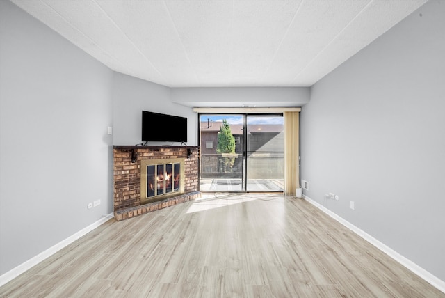 unfurnished living room featuring light hardwood / wood-style floors, a textured ceiling, and a brick fireplace