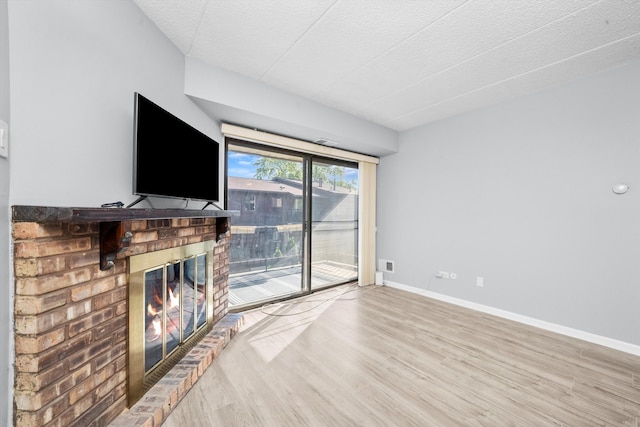 unfurnished living room with light hardwood / wood-style floors, a textured ceiling, and a brick fireplace