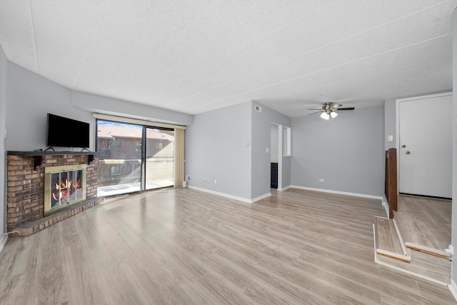 living room with ceiling fan, a textured ceiling, light hardwood / wood-style flooring, and a fireplace