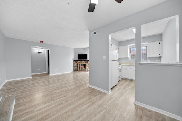 unfurnished living room featuring a brick fireplace, a textured ceiling, light wood-type flooring, and ceiling fan