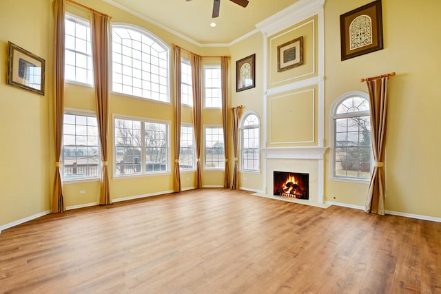 unfurnished living room with light wood-type flooring, ornamental molding, ceiling fan, a healthy amount of sunlight, and a premium fireplace