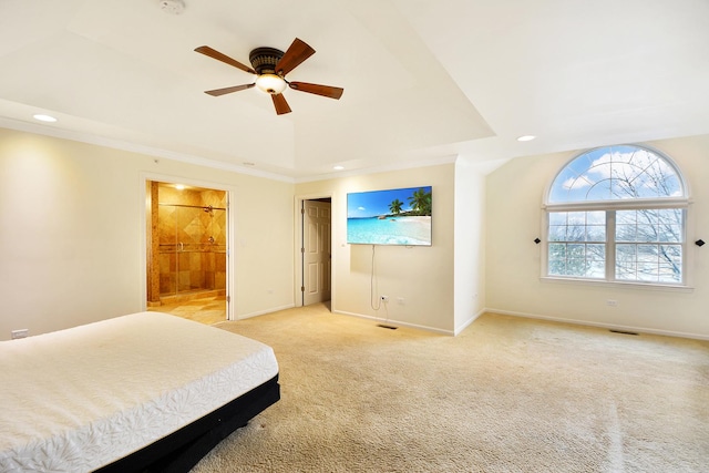 bedroom featuring crown molding, ceiling fan, ensuite bathroom, light colored carpet, and a raised ceiling