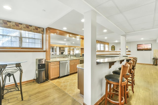 kitchen featuring stainless steel dishwasher, light stone counters, a kitchen breakfast bar, and light hardwood / wood-style flooring