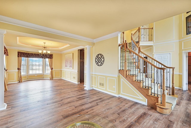 interior space with hardwood / wood-style floors, decorative columns, ornamental molding, a raised ceiling, and a chandelier