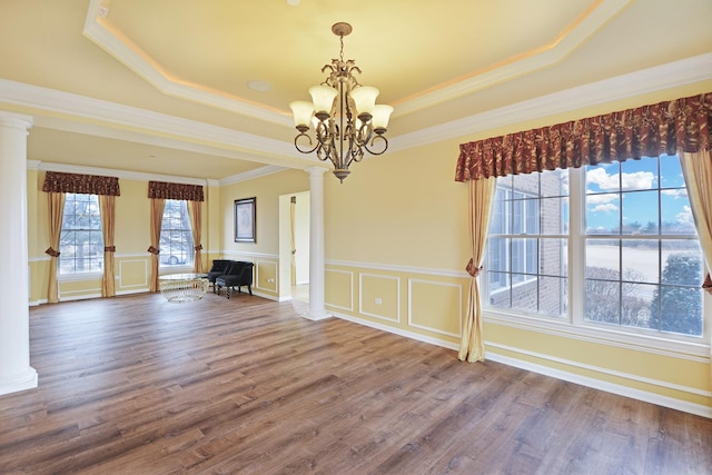 interior space with decorative columns, a notable chandelier, a tray ceiling, wood-type flooring, and ornamental molding