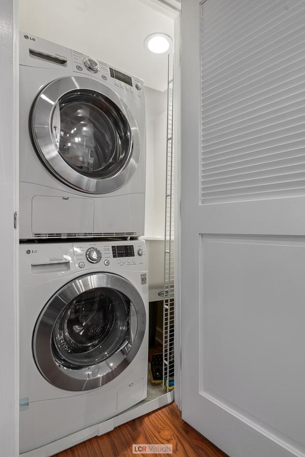 clothes washing area with stacked washing maching and dryer and wood finished floors