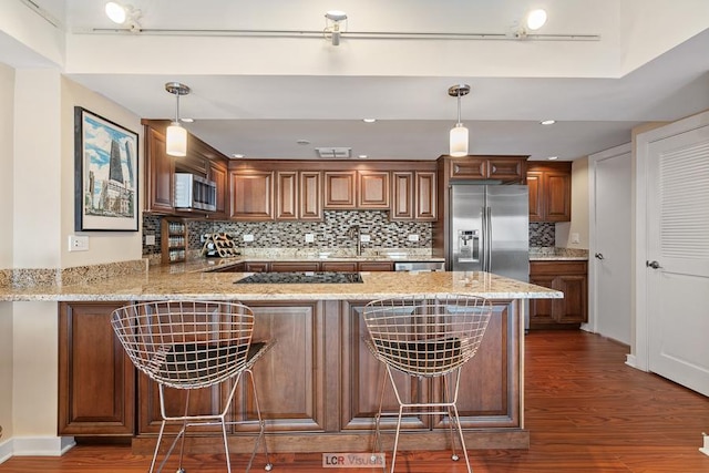 kitchen featuring light stone counters, dark wood-style flooring, a peninsula, stainless steel appliances, and a sink