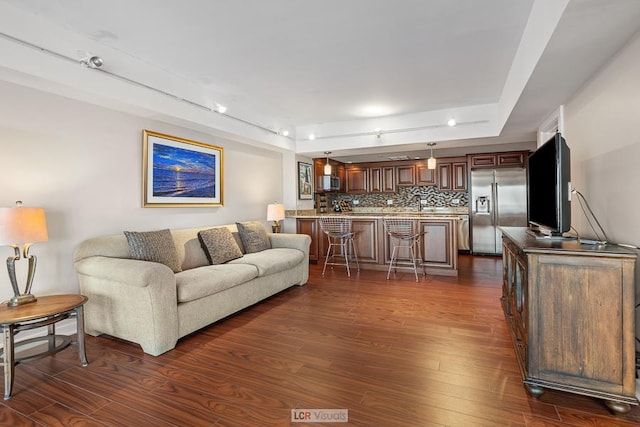 living room with indoor wet bar, a tray ceiling, and dark wood-style flooring