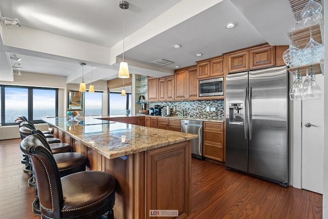 kitchen with light stone counters, brown cabinets, dark wood finished floors, stainless steel appliances, and tasteful backsplash