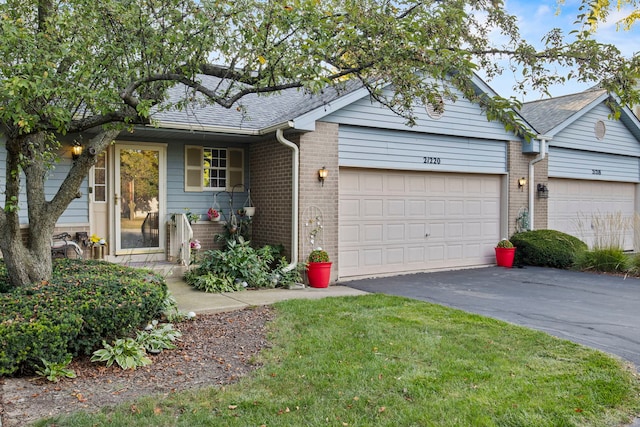 ranch-style home featuring brick siding, aphalt driveway, a garage, and roof with shingles