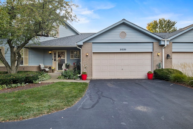 ranch-style house featuring brick siding, an attached garage, aphalt driveway, and roof with shingles